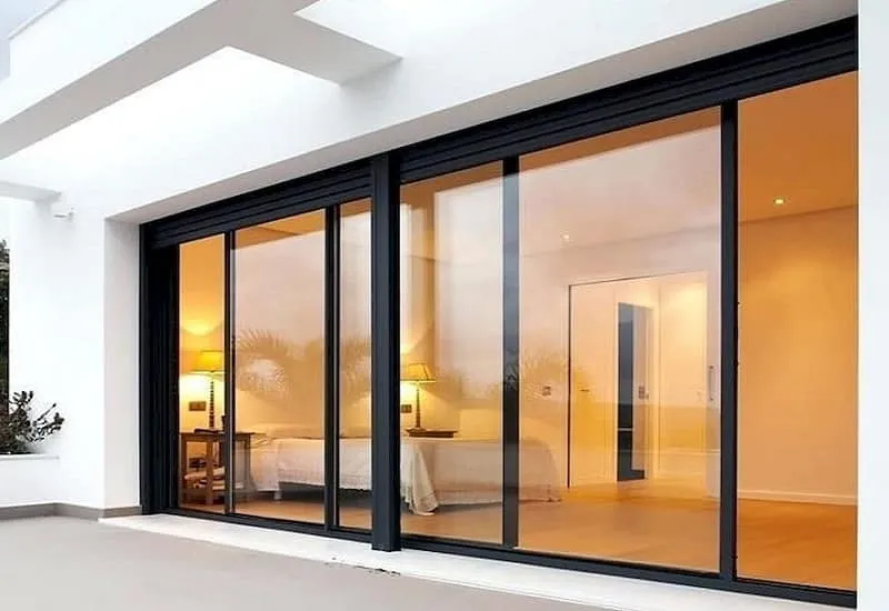 Brede schuifpui met zwarte aluminium profielen in een witte, moderne woning, van buitenaf gezien