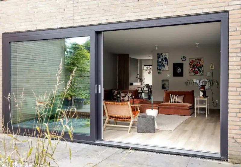 Donkergrijze schuifpui in een bakstenen gevel, half geopend naar een terras met planten